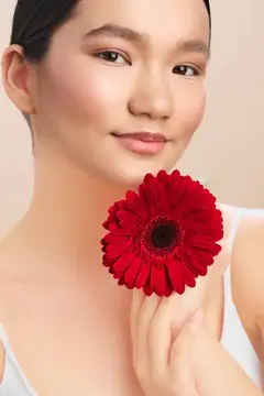 Азиатская девушка с красной герберой у лица