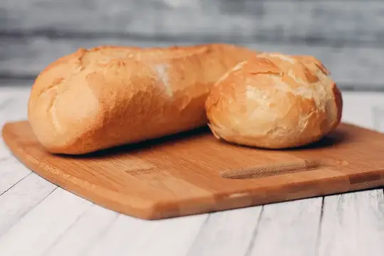 Буханка и булочка — свежая домашняя выпечка на деревянной доске, передающая аромат свежести