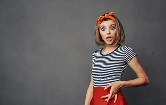 Удивлённая девушка с рыжим платком на голове на сером фоне