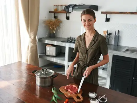 Женщина на кухне улыбается и готовит ужин из мяса и овощей на деревянном столе на фоне стильной кухни, образ жизни