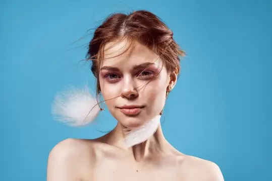 Женщина с обнажёнными плечами, пушистыми серьгами, косметикой на роскошном синем фоне