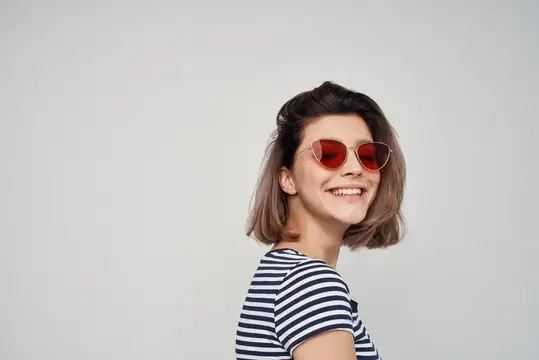 Улыбающаяся девушка в красных солнцезащитных очках на сером фоне