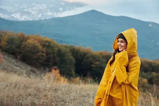 Улыбающаяся девушка в жёлтом дождевике на фоне осенних гор