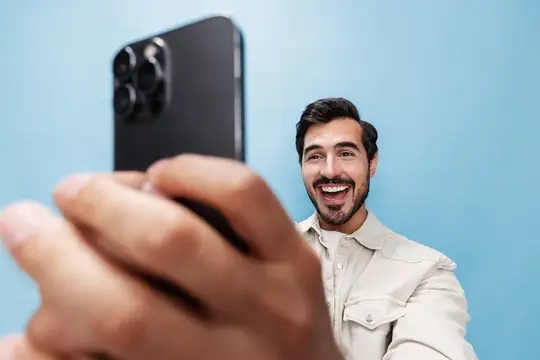 Улыбающийся бородатый мужчина делает селфи на смартфон на голубом фоне