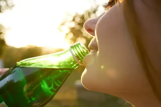 Веселая женщина на природе пьет воду из бутылки, освежающий напиток