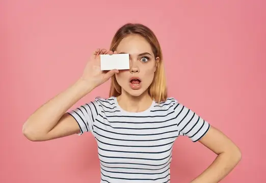 Удивлённая девушка с белой карточкой у глаза на розовом фоне