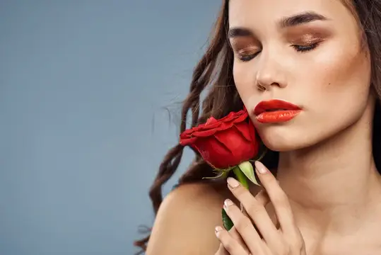Молодая женщина с красной розой у лица на серо-голубом фоне