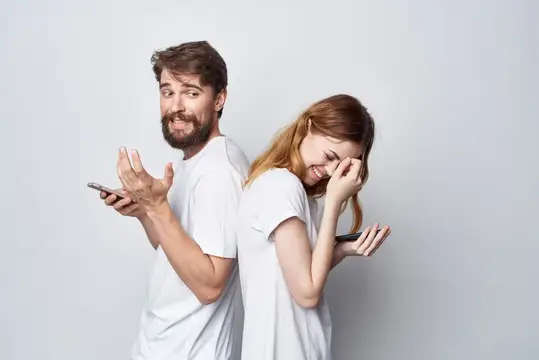 Мужчина и рыжеволосая женщина со смартфонами стоят спина к спине