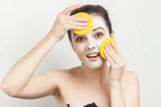 Улыбающаяся девушка с белой маской на лице и жёлтыми спонжами