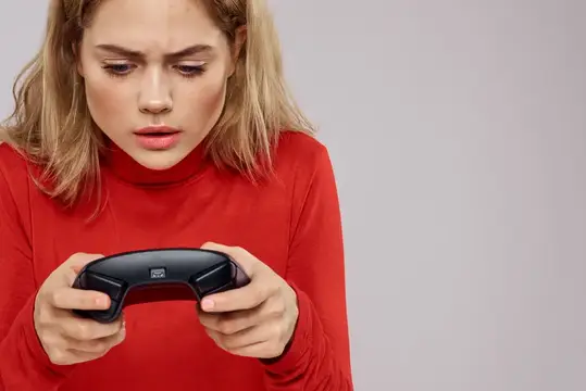 Светловолосая девушка в красном свитере сосредоточенно играет в видеоигру