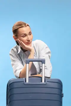 Задумчивая светловолосая женщина опирается на чемодан на голубом фоне
