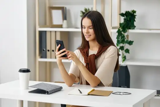 Улыбающаяся девушка со смартфоном за рабочим столом в офисе