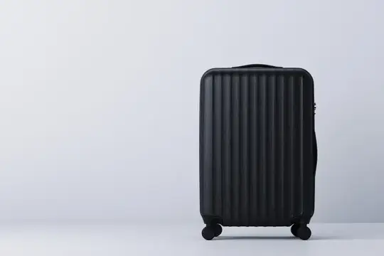 Черный пластиковый чемодан на колесиках стоит у светлой стены