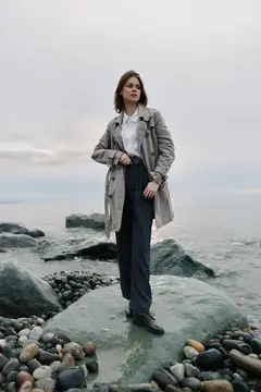 Молодая женщина в плаще стоит на камне у моря