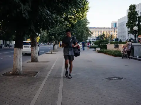 Темнокожий парень с рюкзаком идёт по городской улице, глядя в телефон