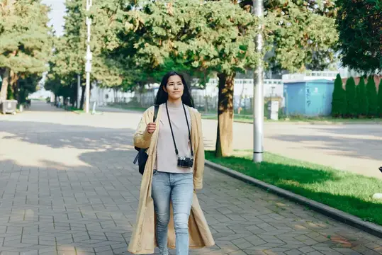 Молодая азиатская девушка с фотокамерой гуляет по аллее в парке