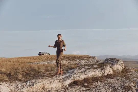 Женщина стоит на камне на фоне автомобиля