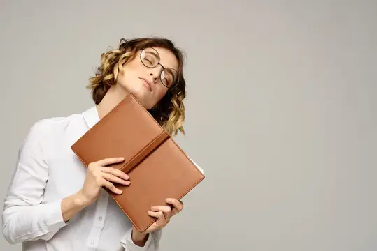 Уставшая женщина в очках прижимает к себе две коричневые книги