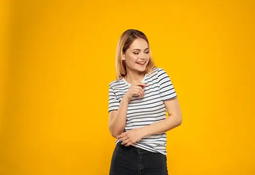 Светловолосая девушка в полосатой футболке улыбается на жёлтом фоне