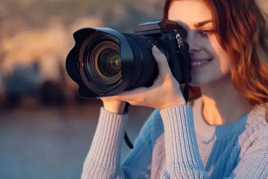 Рыжеволосая девушка с фотокамерой улыбается на закате