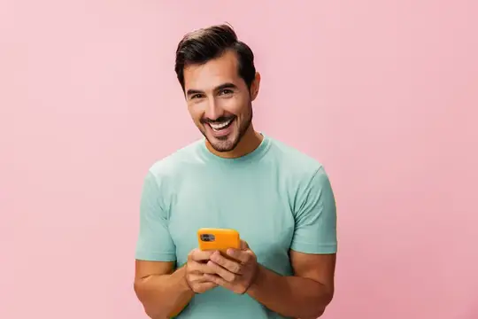 Улыбающийся темноволосый мужчина с телефоном на розовом фоне