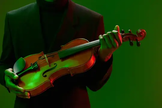 Музыкант в тёмном костюме держит скрипку на зелёном фоне
