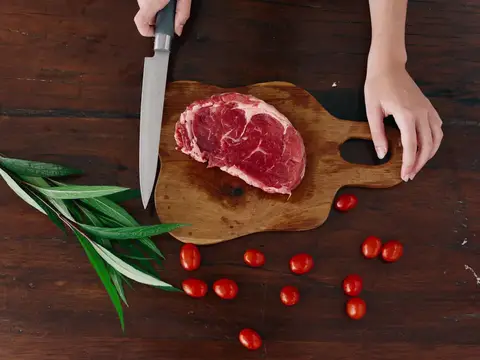 Женщина с ножом в руке нарезает свежее мясо стейка для жарки на кухне