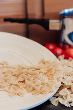 Сырые макароны бантики на белой тарелке на кухне