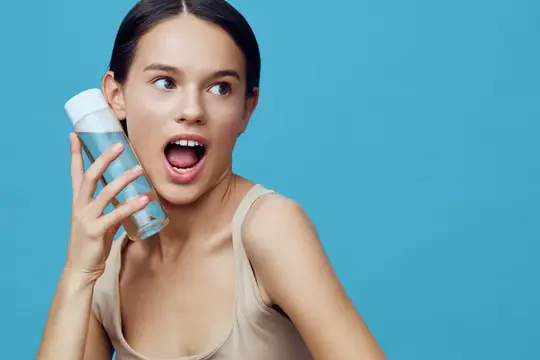 Удивлённая девушка с флаконом косметики на голубом фоне