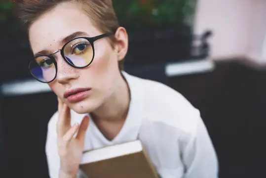 Образованная женщина в очках с книгой сидит за столом