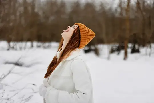Счастливая молодая женщина в зимней одежде и шапке, веселый зимний пейзаж, зимние каникулы