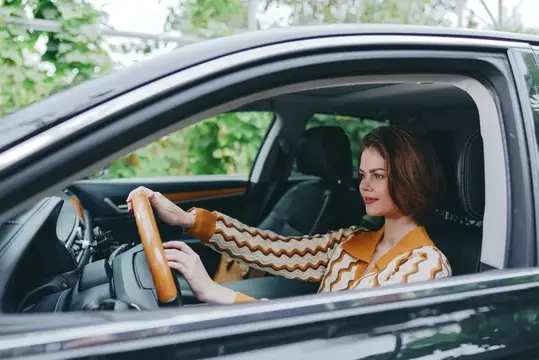 Молодая женщина в полосатой кофте за рулём автомобиля