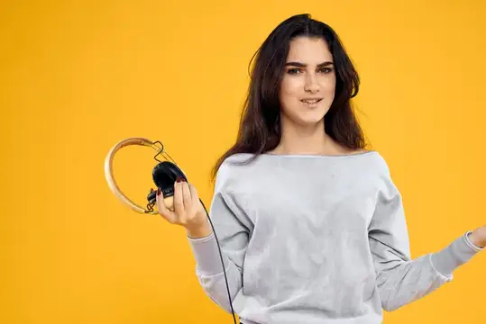 Молодая брюнетка с наушниками в руке на жёлтом фоне