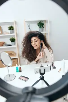 Кудрявая девушка записывает видео о макияже на смартфон