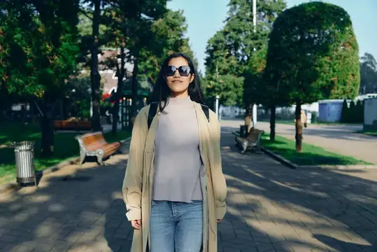 Молодая темноволосая женщина в солнечных очках гуляет по аллее парка