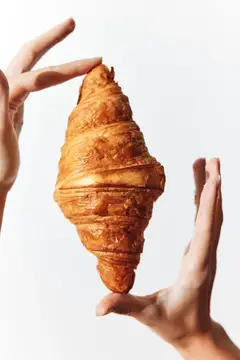 Руки держат румяный круассан на белом фоне