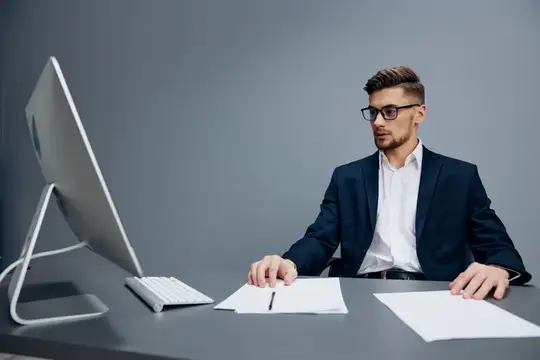 Молодой мужчина в очках и деловом костюме работает за компьютером в офисе