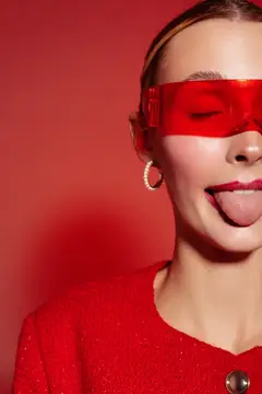 Девушка в красных очках с высунутым языком на красном фоне