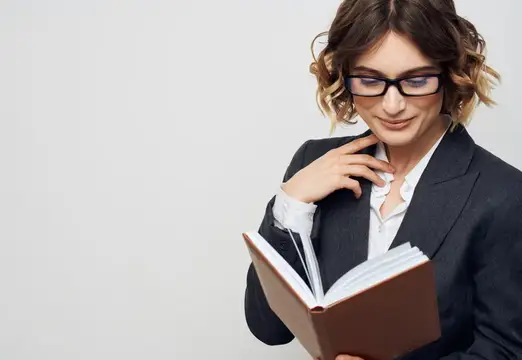 Молодая женщина в очках и деловом костюме читает книгу