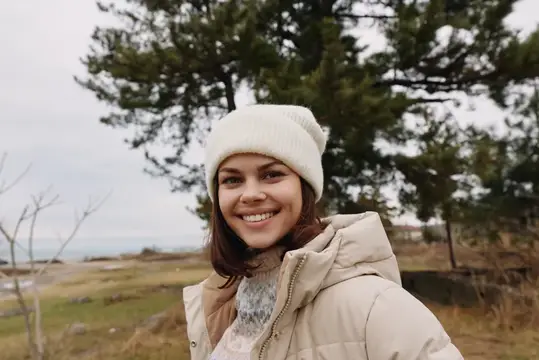Улыбающаяся девушка в белой шапке на фоне сосен
