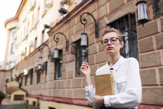Девушка в очках с бумажным пакетом на фоне старинного здания