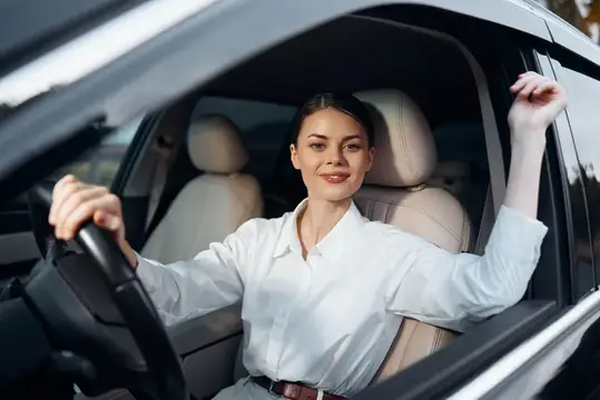 Улыбающаяся женщина в белой рубашке за рулём автомобиля