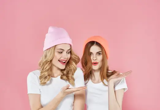 Две улыбающиеся девушки в розовых шапках на розовом фоне