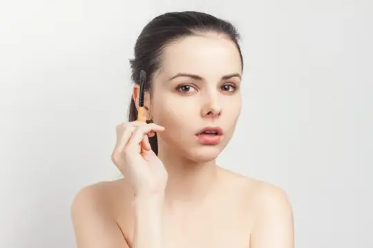 Молодая женщина наносит тени кистью на светлом фоне