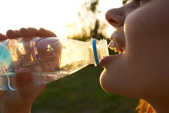 Девушка пьёт воду из пластиковой бутылки на закате