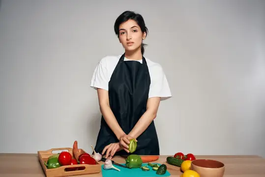 Домохозяйка в черном фартуке на кухне, свежие овощи, здоровая еда