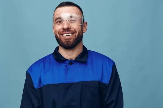 Улыбающийся бородатый мужчина в защитных очках и синей спецодежде
