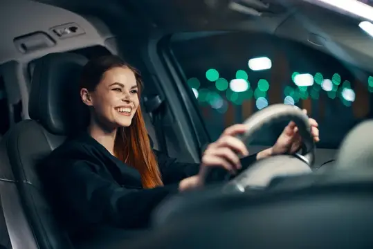 Улыбающаяся рыжеволосая девушка за рулём автомобиля ночью