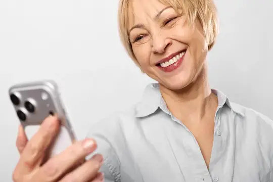 Пожилая женщина улыбается, делая селфи на смартфон на белом студийном фоне