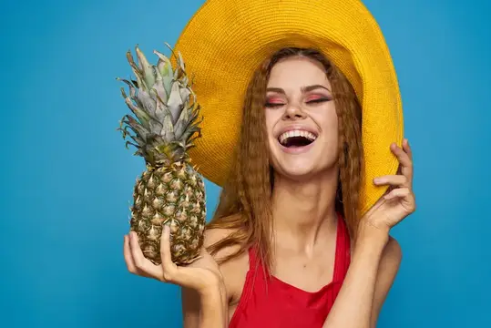 Смеющаяся девушка в жёлтой шляпе с ананасом на синем фоне